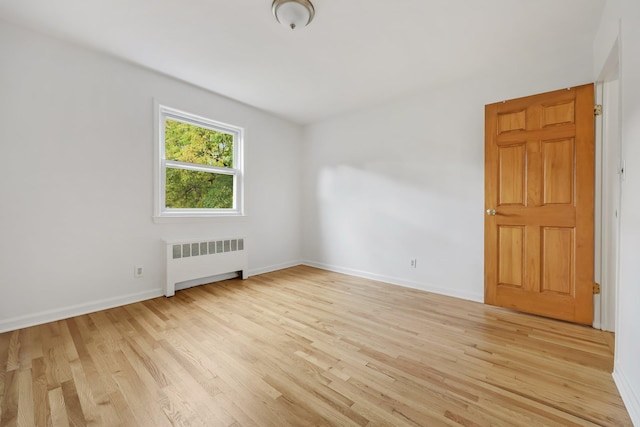 spare room with baseboards, light wood finished floors, and radiator