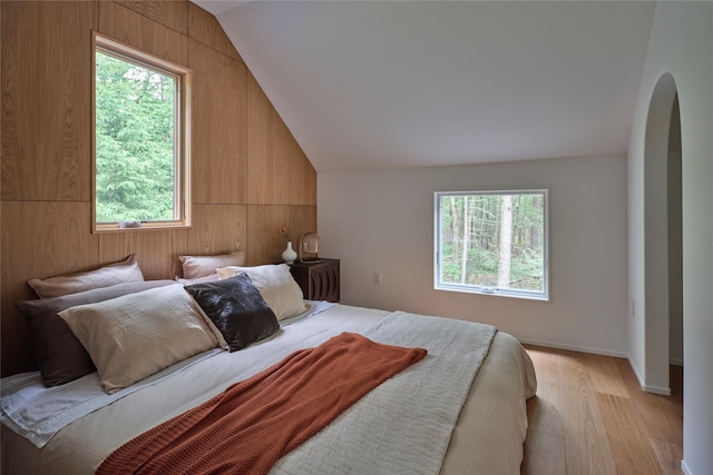 64 Hoyt Rd, Glen Spey, NY 12737 - bedroom featuring arched walkways, multiple windows, vaulted ceiling, light wood-style flooring, and wooden walls