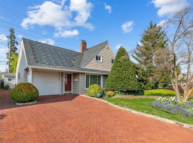 view of front of house with a chimney, decorative driveway, an attached garage, and roof with shingles