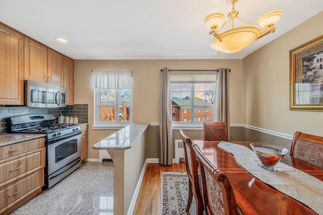 kitchen with decorative backsplash, pendant lighting, appliances with stainless steel finishes, light stone countertops, and baseboards