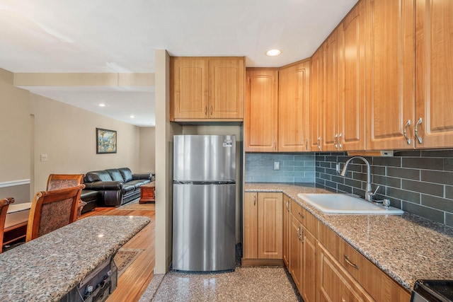 kitchen with freestanding refrigerator, decorative backsplash, light stone countertops, recessed lighting, and a sink