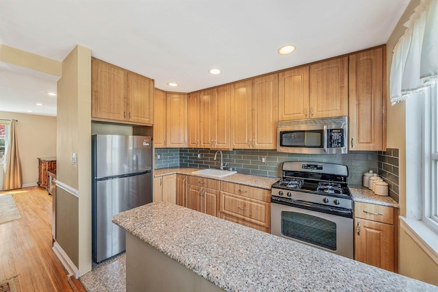 kitchen with backsplash, a sink, baseboards, light stone counters, and stainless steel appliances
