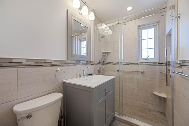 bathroom featuring vanity, toilet, a wainscoted wall, tile walls, and a shower stall