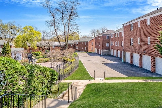 view of home's community featuring an attached garage, fence, a lawn, driveway, and a residential view