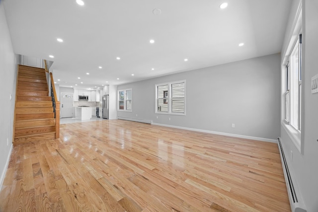 unfurnished living room with baseboard heating, a baseboard radiator, stairway, light wood-type flooring, and recessed lighting