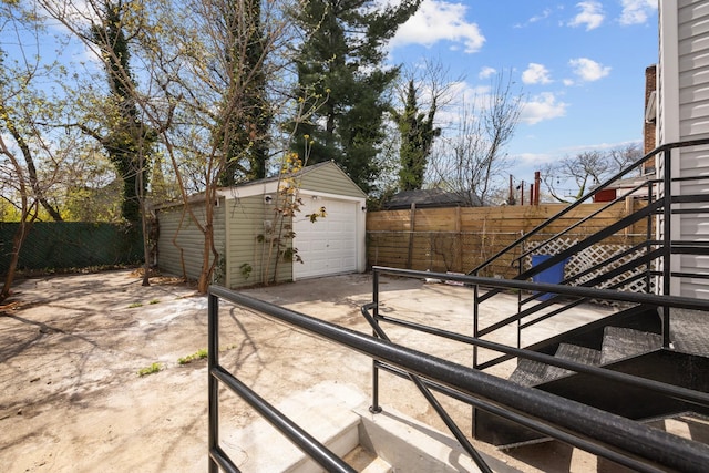 view of patio featuring an outbuilding, a fenced backyard, driveway, a garage, and stairway