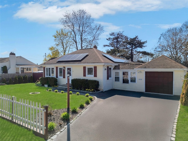 ranch-style house with fence, aphalt driveway, solar panels, a front lawn, and an attached garage