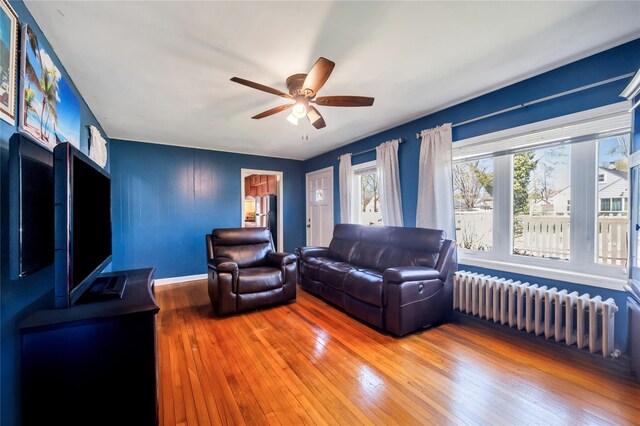 living room featuring wood-type flooring, a ceiling fan, radiator heating unit, and baseboards