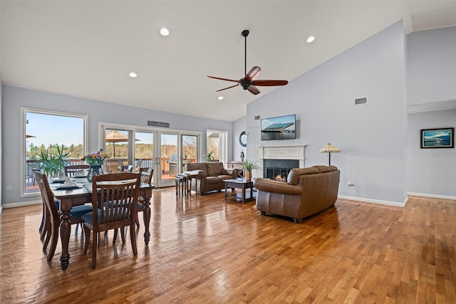 dining space featuring baseboards, ceiling fan, a lit fireplace, and high vaulted ceiling