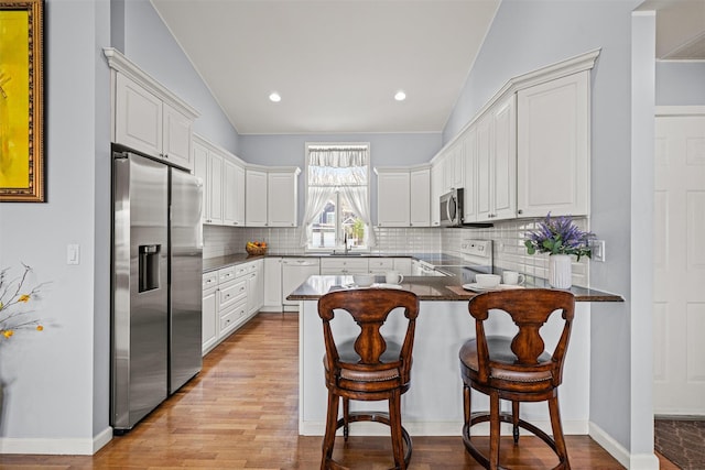 kitchen featuring appliances with stainless steel finishes, vaulted ceiling, a sink, light wood finished floors, and a peninsula