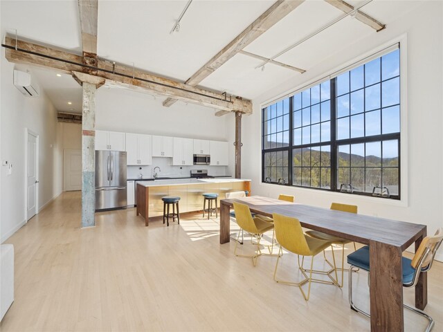 dining space with light wood-style flooring, a high ceiling, a wall unit AC, and beam ceiling
