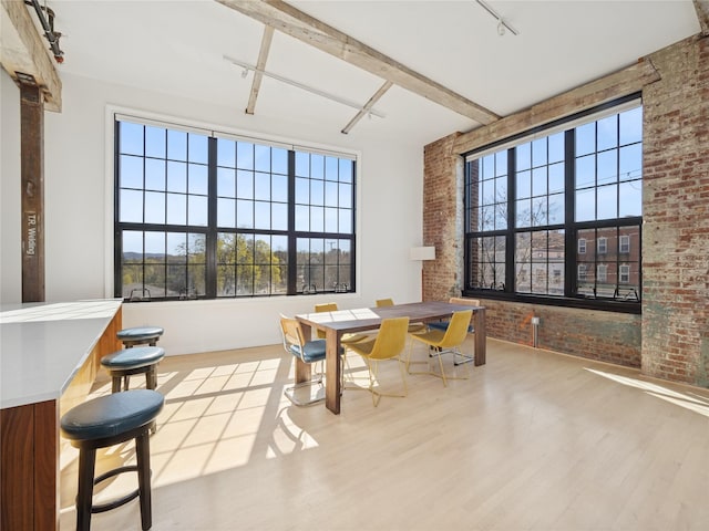 dining area with track lighting, wood finished floors, brick wall, and plenty of natural light