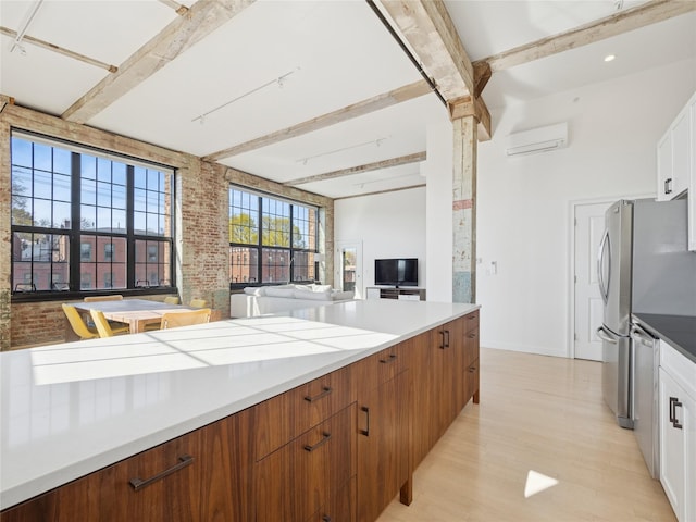 kitchen with white cabinetry, light wood-style flooring, beamed ceiling, brick wall, and a wall mounted air conditioner