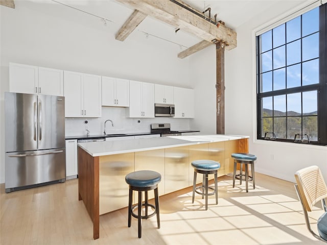 kitchen featuring a high ceiling, beam ceiling, stainless steel appliances, tasteful backsplash, and a breakfast bar area