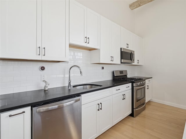 kitchen featuring a sink, tasteful backsplash, white cabinetry, dark countertops, and appliances with stainless steel finishes