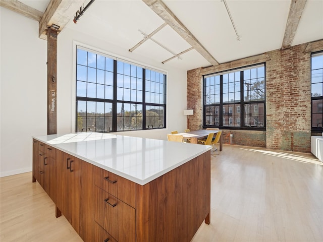kitchen featuring brick wall, light wood-style flooring, and beamed ceiling