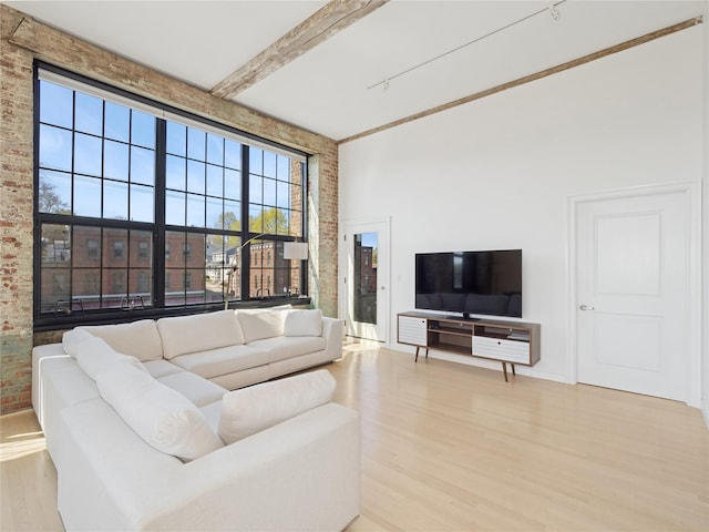 living room with brick wall, a healthy amount of sunlight, a high ceiling, and light wood finished floors