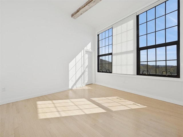 empty room featuring beam ceiling, wood finished floors, a high ceiling, and baseboards