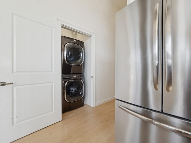 laundry room with baseboards, stacked washing maching and dryer, laundry area, and light wood-style flooring