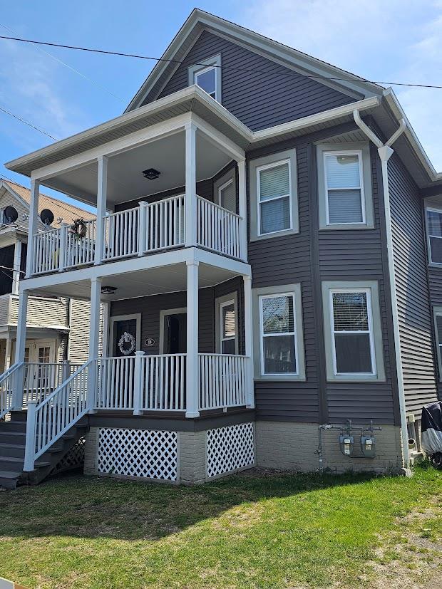 back of property with a porch, a lawn, and a balcony