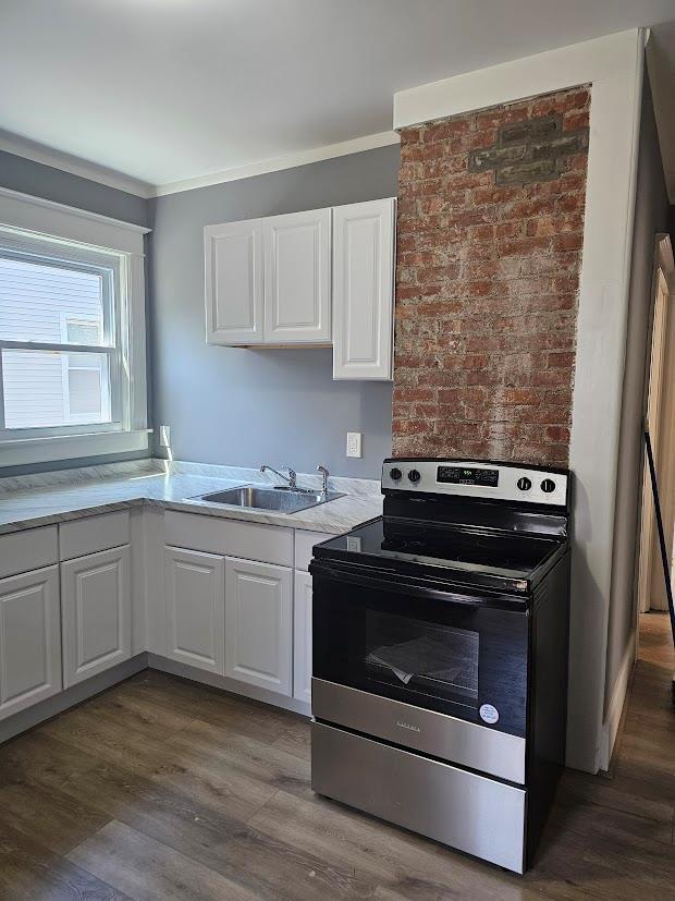 kitchen featuring light countertops, stainless steel range with electric cooktop, white cabinets, and a sink