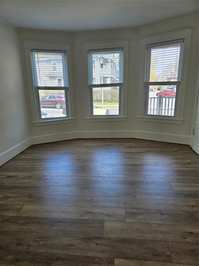 empty room with crown molding, dark wood-style floors, and baseboards
