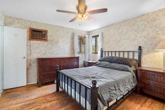 bedroom featuring a ceiling fan, wallpapered walls, a wall mounted AC, and wood finished floors