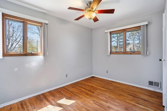 spare room with visible vents, wood finished floors, a healthy amount of sunlight, and baseboards