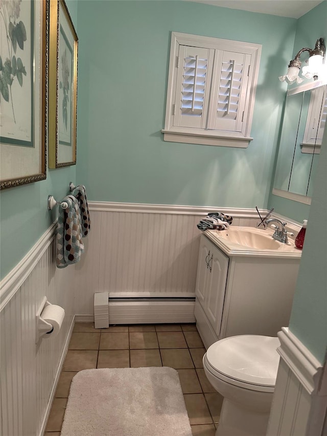 half bathroom with tile patterned flooring, wainscoting, baseboard heating, toilet, and vanity