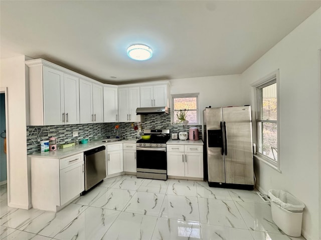 kitchen with a sink, stainless steel appliances, under cabinet range hood, marble finish floor, and light countertops