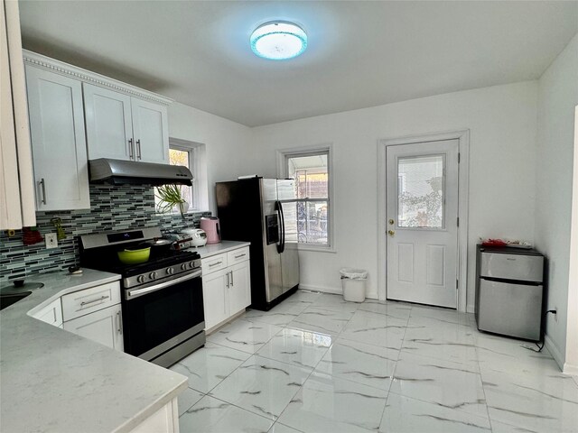 kitchen featuring appliances with stainless steel finishes, decorative backsplash, baseboards, and under cabinet range hood