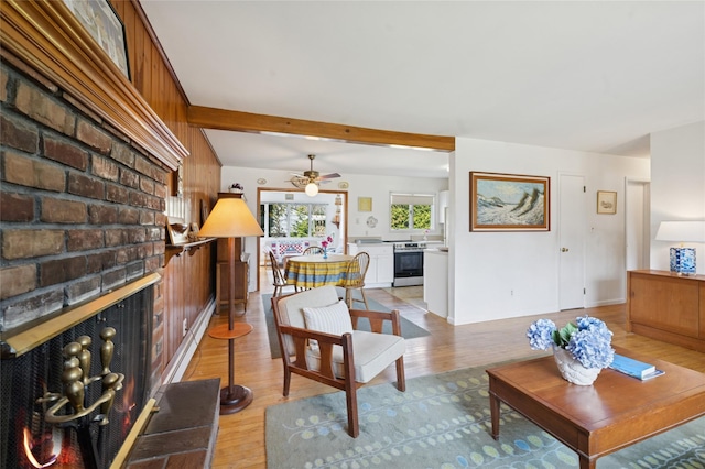 living area featuring light wood-style floors, a ceiling fan, and a brick fireplace