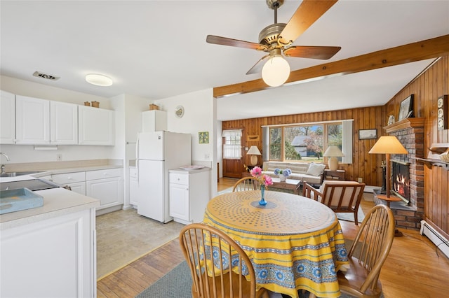 dining space featuring beam ceiling, a fireplace, wooden walls, a ceiling fan, and light wood-style flooring