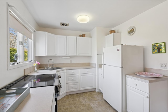 kitchen featuring freestanding refrigerator, range with electric cooktop, light countertops, a sink, and white cabinetry