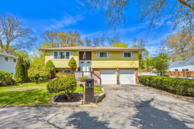 bi-level home featuring a front lawn, driveway, brick siding, an attached garage, and fence