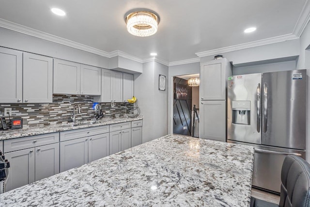 kitchen featuring light stone countertops, a sink, stainless steel fridge, crown molding, and backsplash