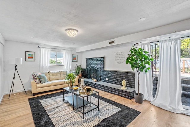 living area with visible vents, light wood-style floors, and a brick fireplace