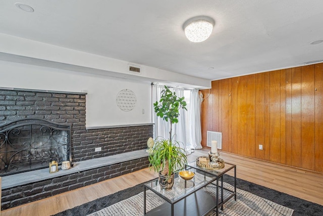 living area with wood walls, wood finished floors, visible vents, and a brick fireplace