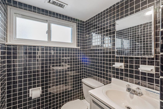 bathroom featuring visible vents, toilet, vanity, and tile walls