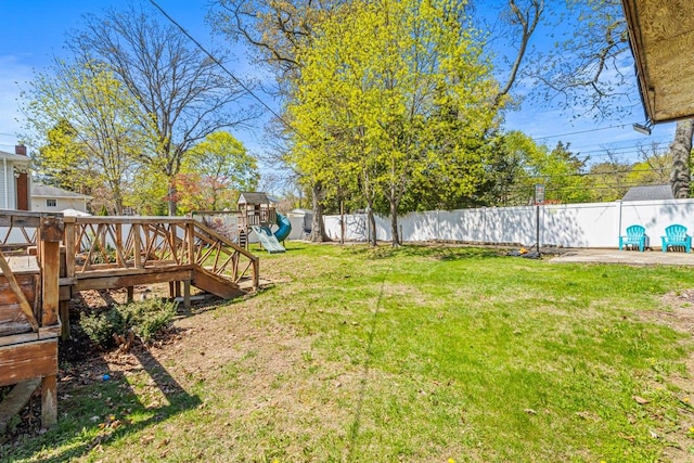 view of yard featuring a wooden deck, a playground, and a fenced backyard