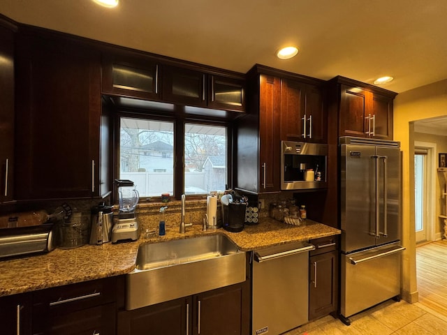 kitchen with dark stone counters, recessed lighting, a sink, stainless steel appliances, and dark brown cabinetry