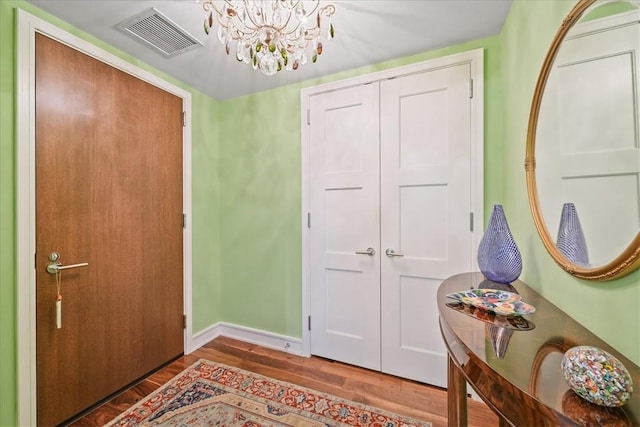 foyer with visible vents, wood finished floors, a chandelier, and baseboards