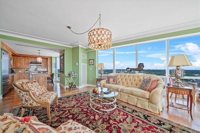 living room with an inviting chandelier, wood finished floors, ornamental molding, and baseboards