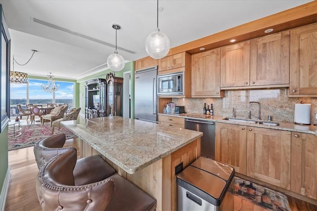 kitchen with decorative backsplash, a chandelier, a breakfast bar area, built in appliances, and a sink