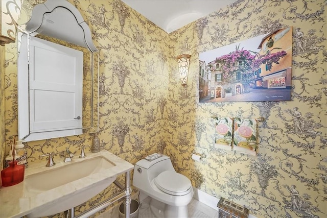 bathroom featuring toilet, a sink, and wallpapered walls