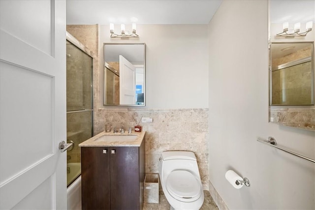 bathroom with bath / shower combo with glass door, vanity, toilet, and tile walls