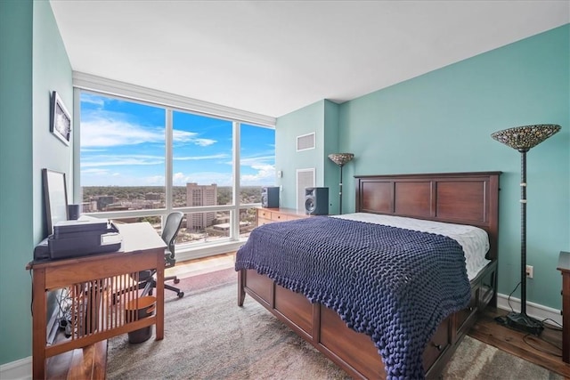 bedroom featuring a wall of windows, wood finished floors, and baseboards