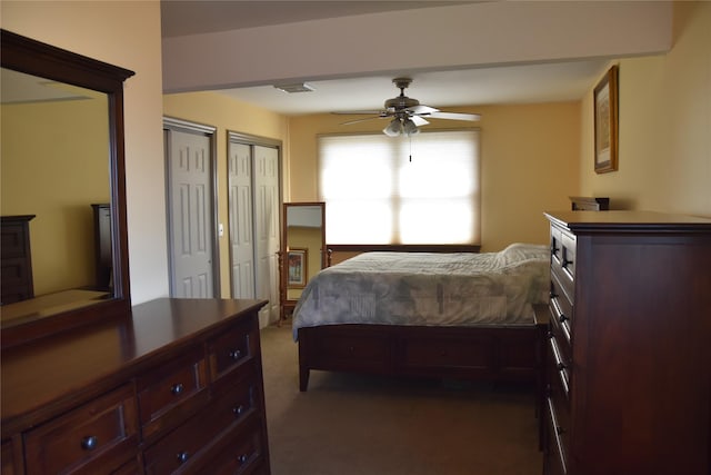 bedroom featuring two closets, a ceiling fan, visible vents, and dark carpet