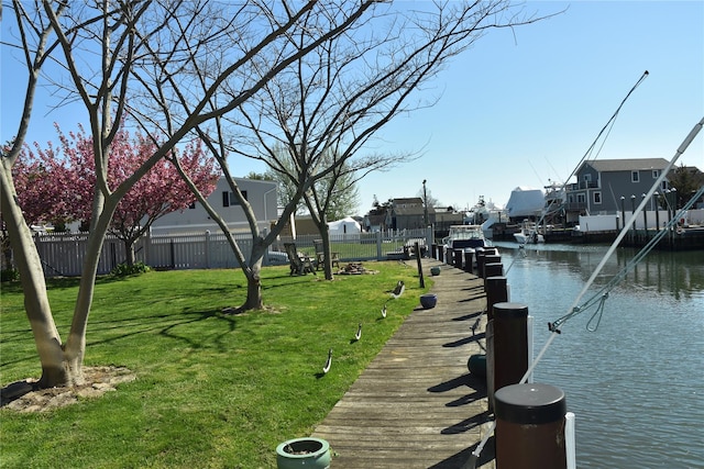 view of dock featuring a lawn, fence, a water view, and a residential view