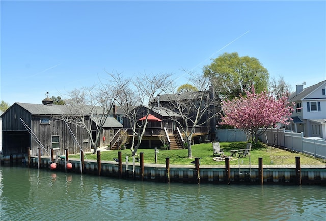 dock area with a deck with water view, fence, a lawn, and stairway